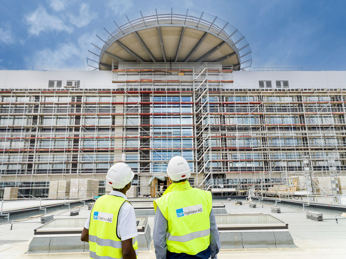 Zwei Bauingenieure mit Schutzhelmen inspizieren eine große Baustelle.